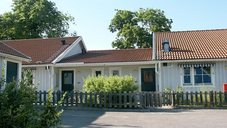 Buskar och staket i förgrunden. Ljusgrå förskola med tegeltak.