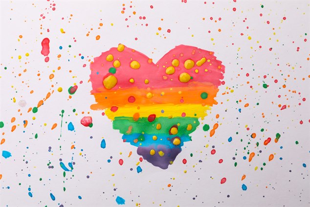 Ett målat regnbågshjärta mot en prickig bakgrund.