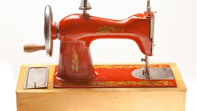 en liten röd symaskin av gammal modell, utsirat mönster i guld på sidorna och plattan