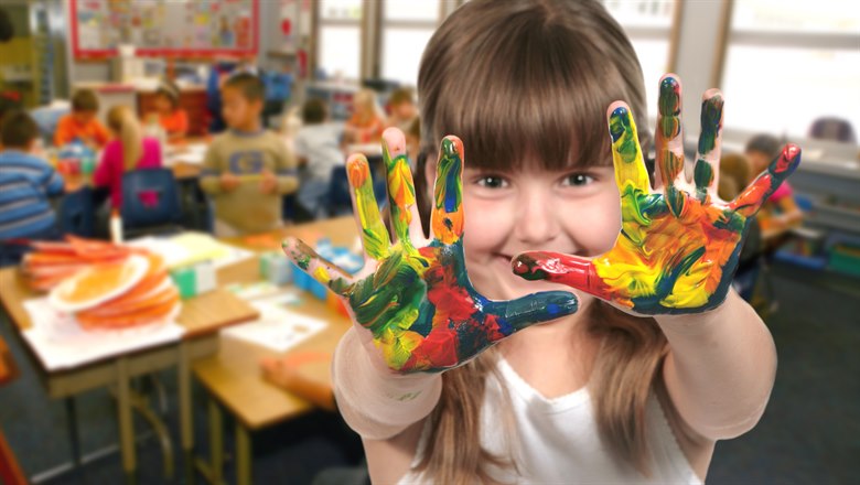 En flicka står i klassrum med sina målarfärgskladdiga handflator mot kameran.