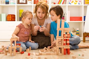 En förskolepedagog sitter på golvet och bygger träkonstruktioner tillsammans med två barn