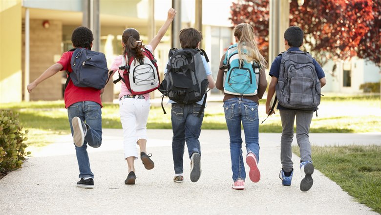 Fem skolbarn med ryggsäckar är på väg mot skolbyggnaden