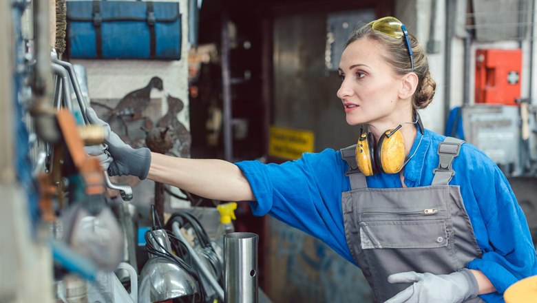 Kvinna i industriarbete tar verktyg från vägg