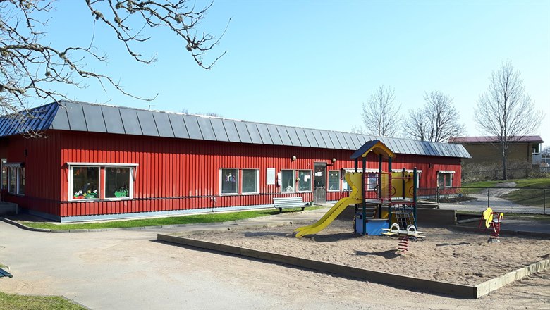 Förskolans röda hus med en sandlåda med rutschkana och gunghästar framför