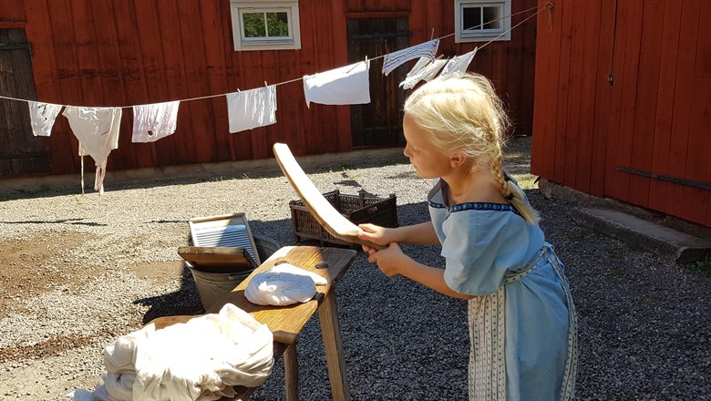 Flicka tvättar kläder utomhus i solen på gammaldags vis