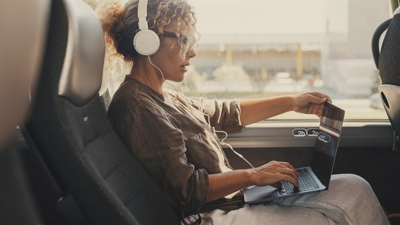 Kvinna sitter med hörlurar och laptop på en buss.