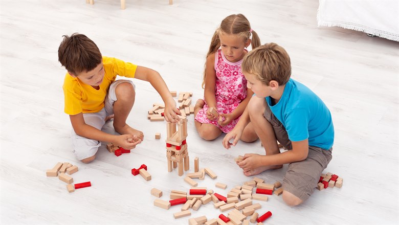 Tre barn sitter på golvet i en förskola och bygger med klossar, två killar och en tjej.