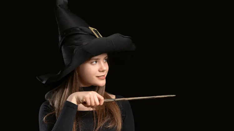 En ung flicka utklädd till trollkarl håller i en trollstav.