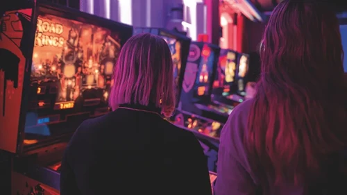 Några kvinnor som står bredvid varandra framför ett flipperspel.