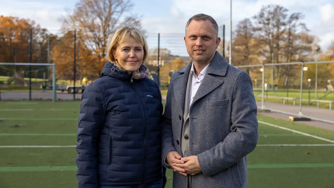 Elisabeth Lundqvist och Stefan Eriksson tittar in i kameran. De står på en basketplan