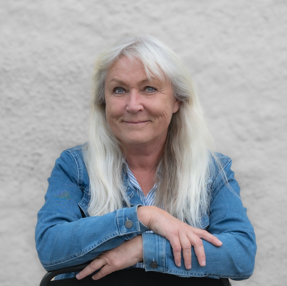 Eva Granlund sitter med armarna framför sig, tittar in i kameran och ler. Hon har en blå jeansjacka, samma färg som hennes ögon.