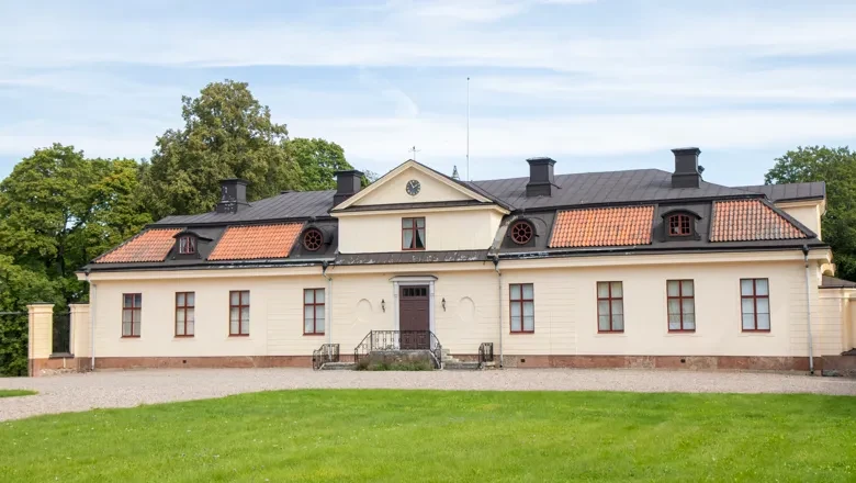 Äldre gul putsad herrgårdsbyggnad bakom gräsmatta