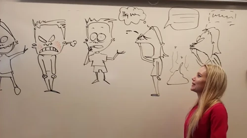 Ung kvinna i röd tröja står framför en whiteboardtavla med tecknade figurer
