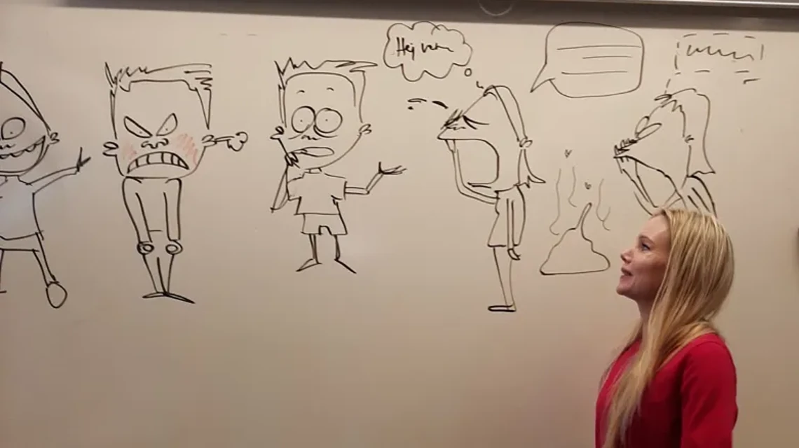 Ung kvinna i röd tröja står framför en whiteboardtavla med tecknade figurer
