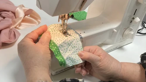 Detaljbild av två händer som syr på en symaskin
