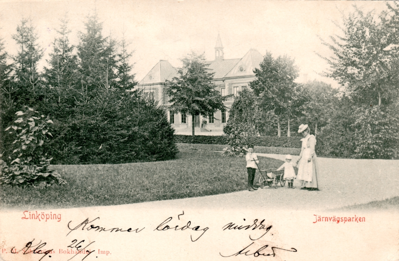 Gammalt vykort med foto från Järnvägsparken. I förgrunden syns kvinna med två små barn och en skrinda. Grönskande park.