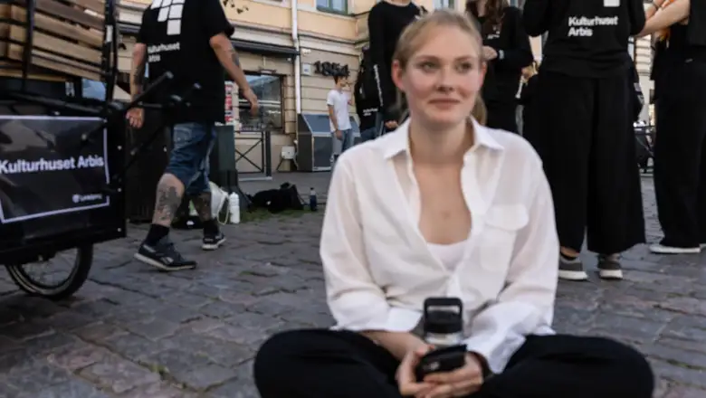 Astrid sitter på marken i skräddarställning. Hon har en vit skjorta och svarta byxor