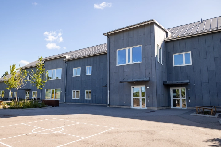 En asfalterad skolgård framför en tvåvåningsbyggnad.