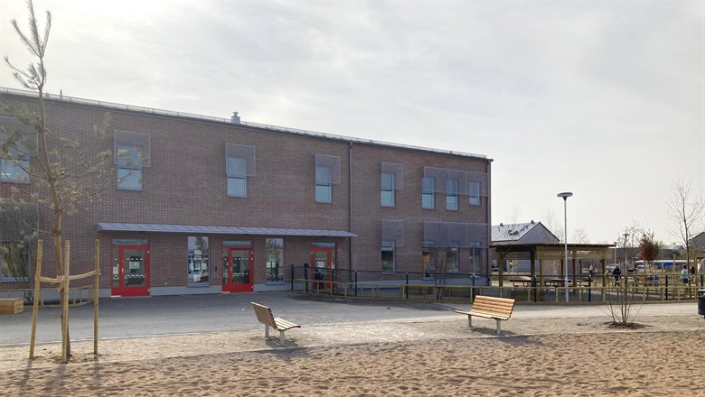 Framsidan av Valkyriagatans förskola som är en tvåvånings tegelklädd byggnad. I förgrunden finns lekplats med sandlåda och bänkar.