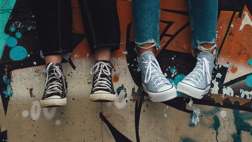 Benen och fötterna på två ungdomar som sitter på en mur med grafitti