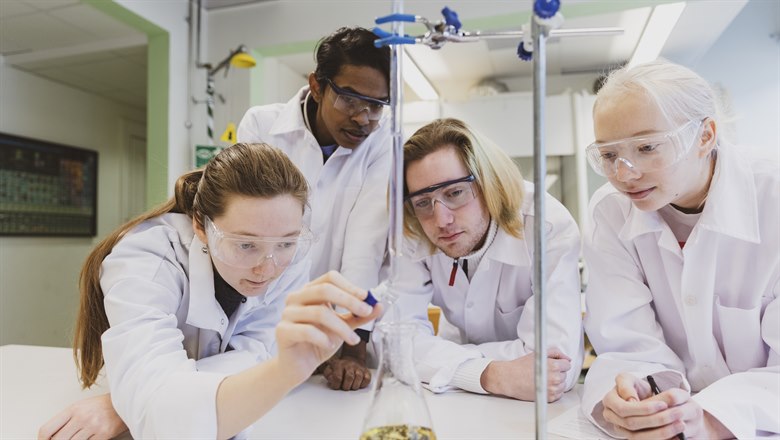 Gymnasieelever med skyddsrockar och glasögon gör kemiexperiment 