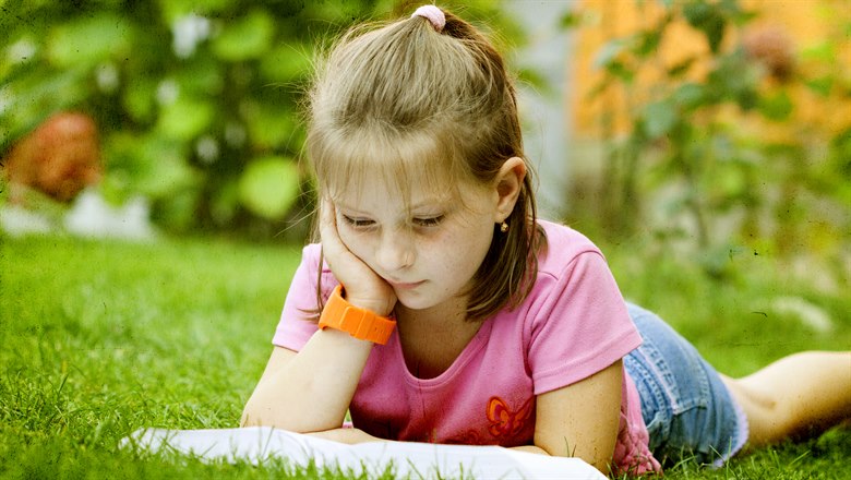 Flicka som läser en bok på gräsmattan.
