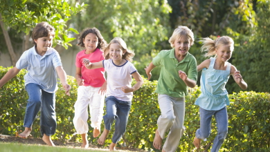 fem glada barn springer barfota mot oss på en gräsmatta med en grön häck