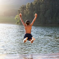 En pojke som hoppar från en brygga ner i en sjö
