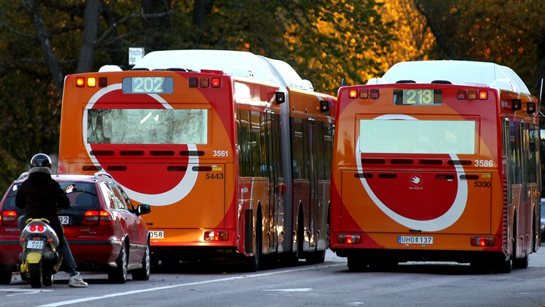 Två orangea bussars baksidor ute i trafiken