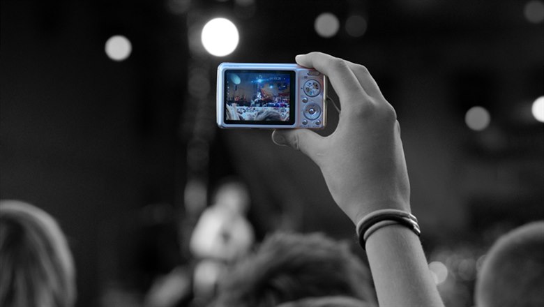En hand i luften som filmar en konsert med en kamera.