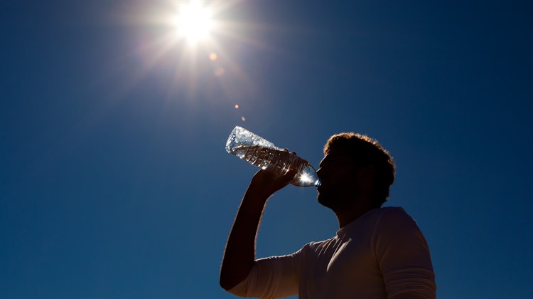 Man dricker vatten ur flaska i solsken med blå himmel som bakgrund.