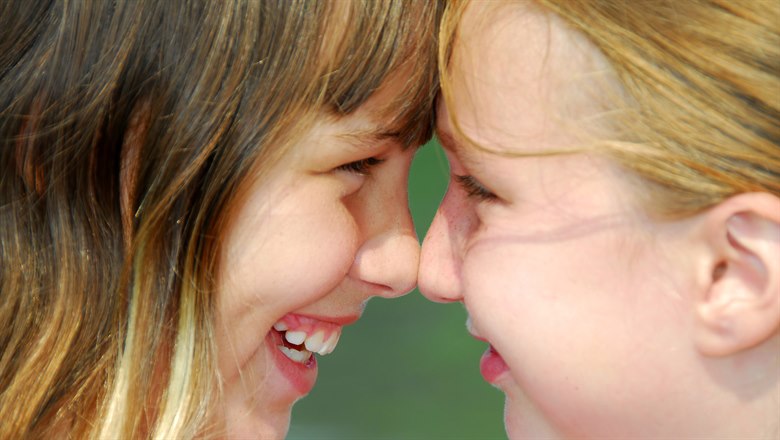 Två flickor som skrattar och lutar panna och näsa mot varandra