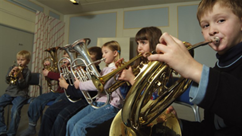 Brasslek Kulturskolan. Sju barn sitter på rad och spelar brassinstrument, såsom valthorn och tuba.