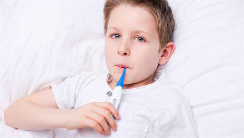 En pojke ligger i en säng och tar tempen med en muntermometer