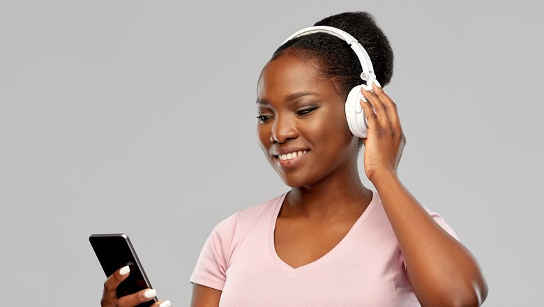 En tjej lyssnar på något i vita hörlurar via mobilen.