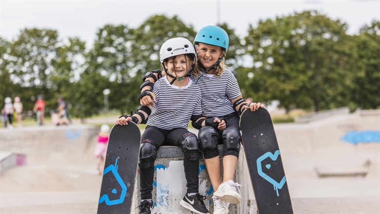 Två barn i en skateboardpark hållandes varsin skateboard. 