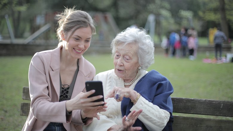 En ung och en äldre kvinna tittar tillsammans på en mobiltelefon.