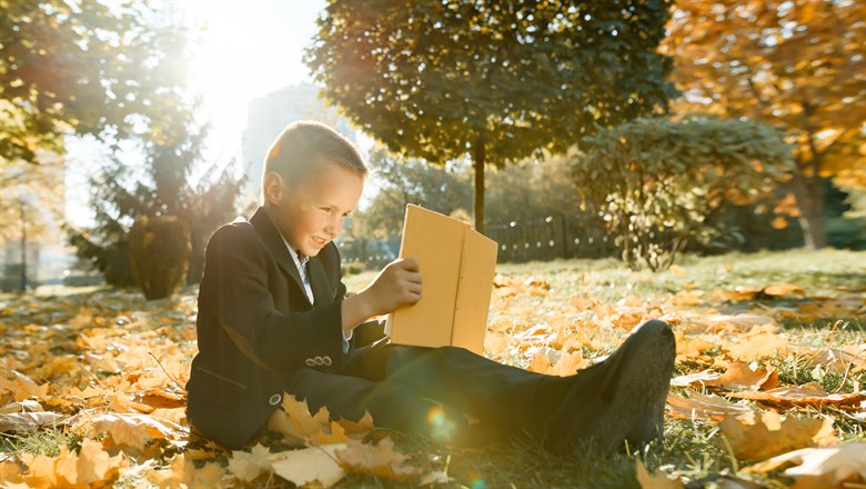 Pojke sitter utomhus och läser bland höstlöv
