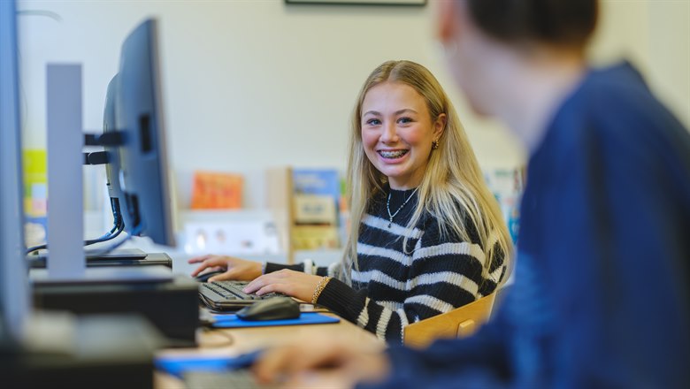 Två studerande elever, en tjej som skriver på datorn och pratar med en klasskompis. 