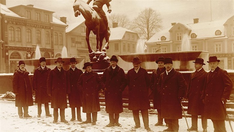En skara män i vinterlandskap framför Folkungabrunnen vid invigningen