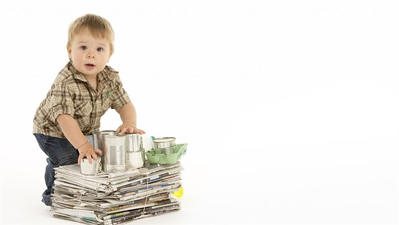 En liten pojke står bakom en trave tidningar och några plåtburkar