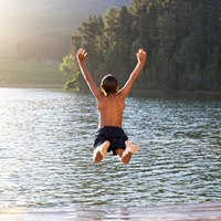En pojke som hoppar från en brygga ner i en sjö