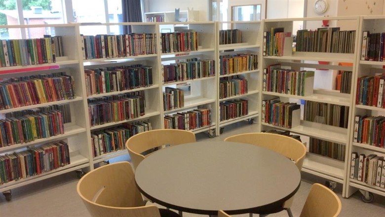 Vy över bibliotekshyllor med ett litet runt bord och stolar i förgrunden.