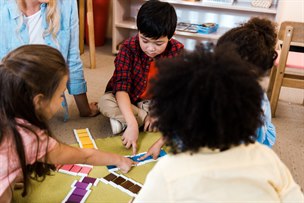 Fyra förskolebarn sitter tillsammans med en förskolepersonal kring ett spel.
