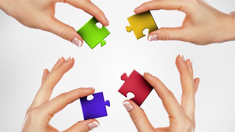 Fyra händer som håller i en varsin pusselbit i olika färger som om de skall sätta ihop pusslet