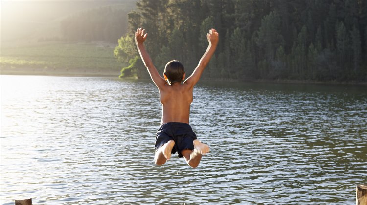 Pojke hopparner  i vattnet i en sjö.