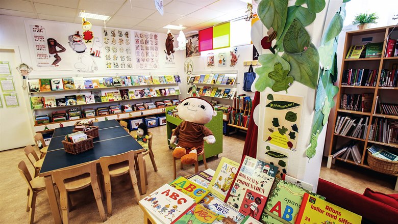En barnhörna med böcker och ett bord där en stor Alfons Åberg-docka sitter