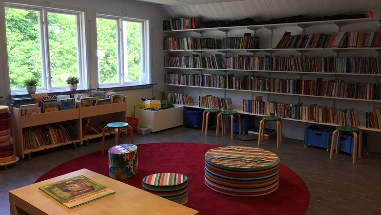 Skolbibliotek med röd matta och färgglada sittpuffar i förgrunden