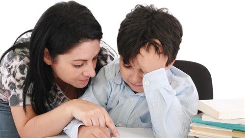 En mamma hjälper sin son med läxorna. Han sitter och mamman böjer sig över hans axel och pekar på något i skrivboken