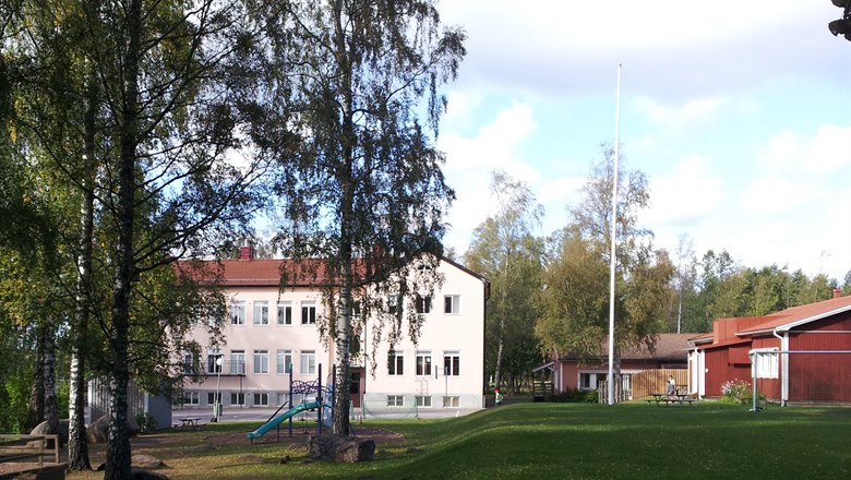 Sätra skola sett från fotbollsplanen, i förgrundern björkar och en rutschkana